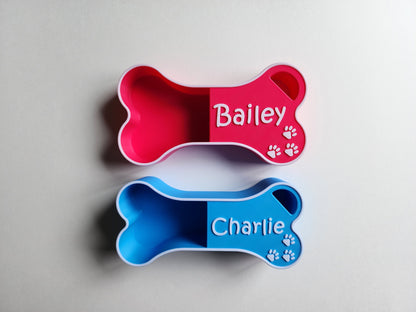 A pink dog food scoop in the shape of a bone with the name Bailey in white. A light blue dog food scoop in the shape of a bone with the name Charlie in white.