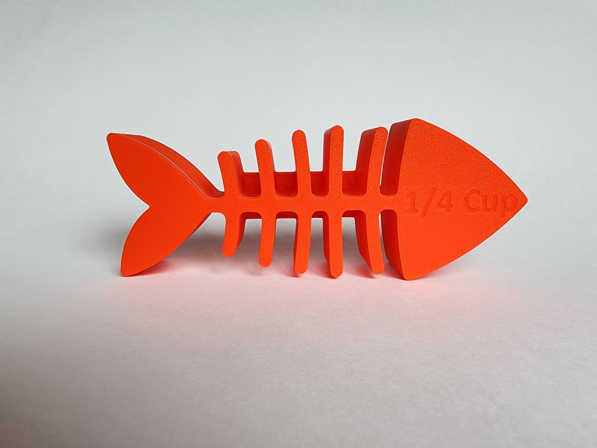 The underside of an orange 1/4 cup cat food scoop shaped like a fish skeleton