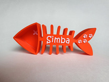 An orange 1/4 cup cat food scoop shaped like a fish skeleton with the name Simba and small paw prints in white