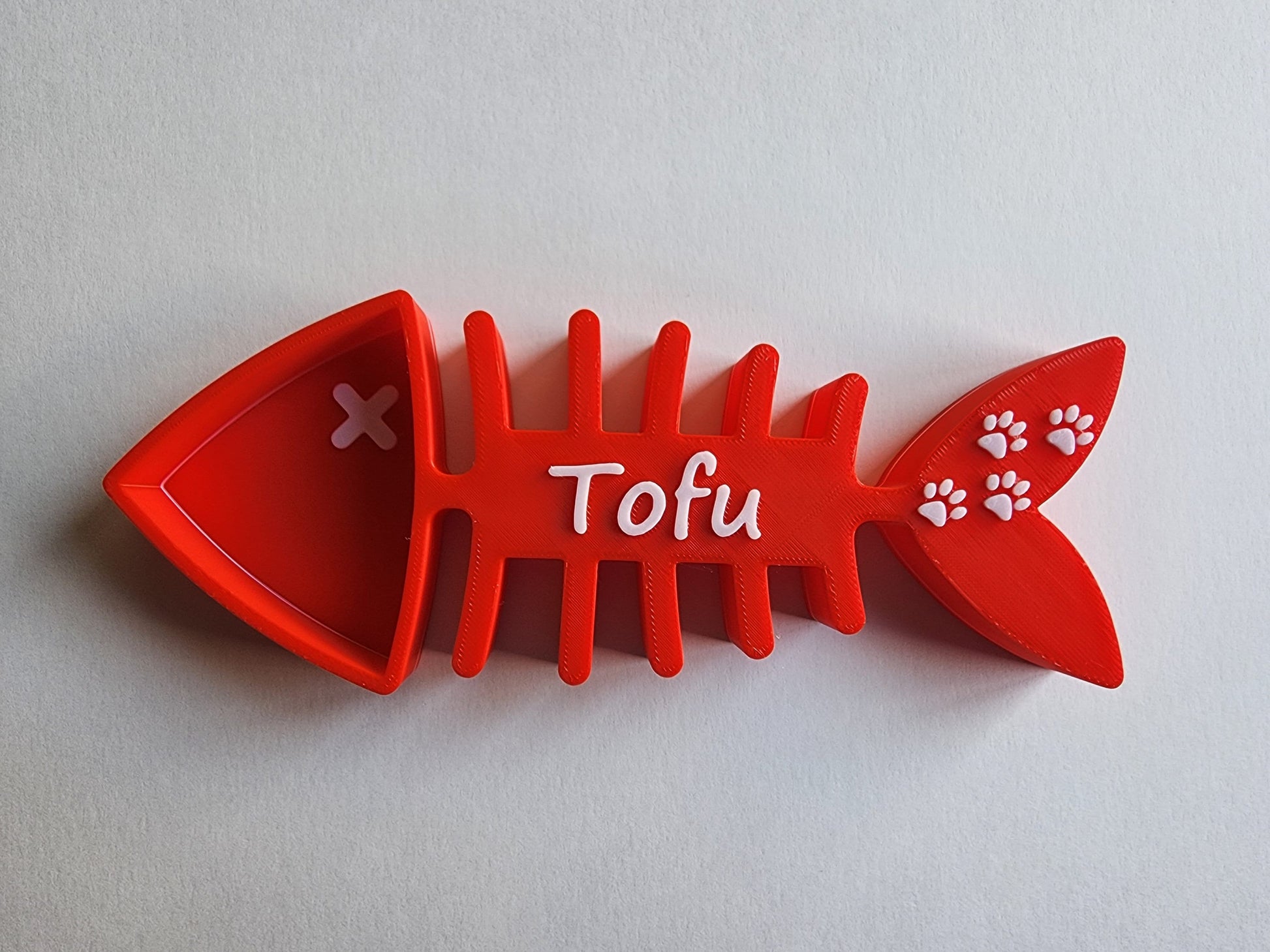 A red 1/8 cup cat food scoop shaped like a fish skeleton with the name Tofu and small paw prints in white