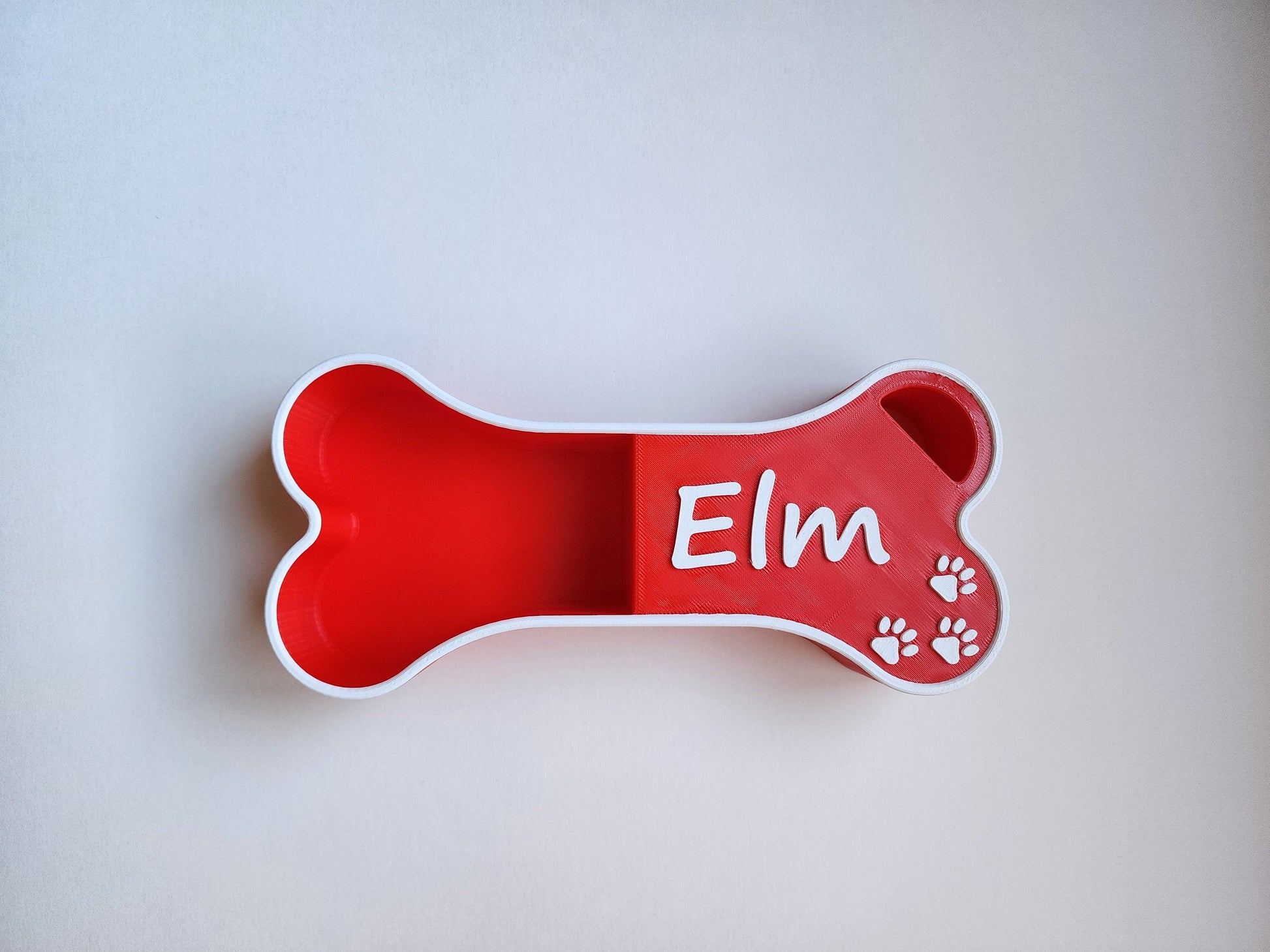 A red dog food scoop in the shape of a bone with the name Elm in white