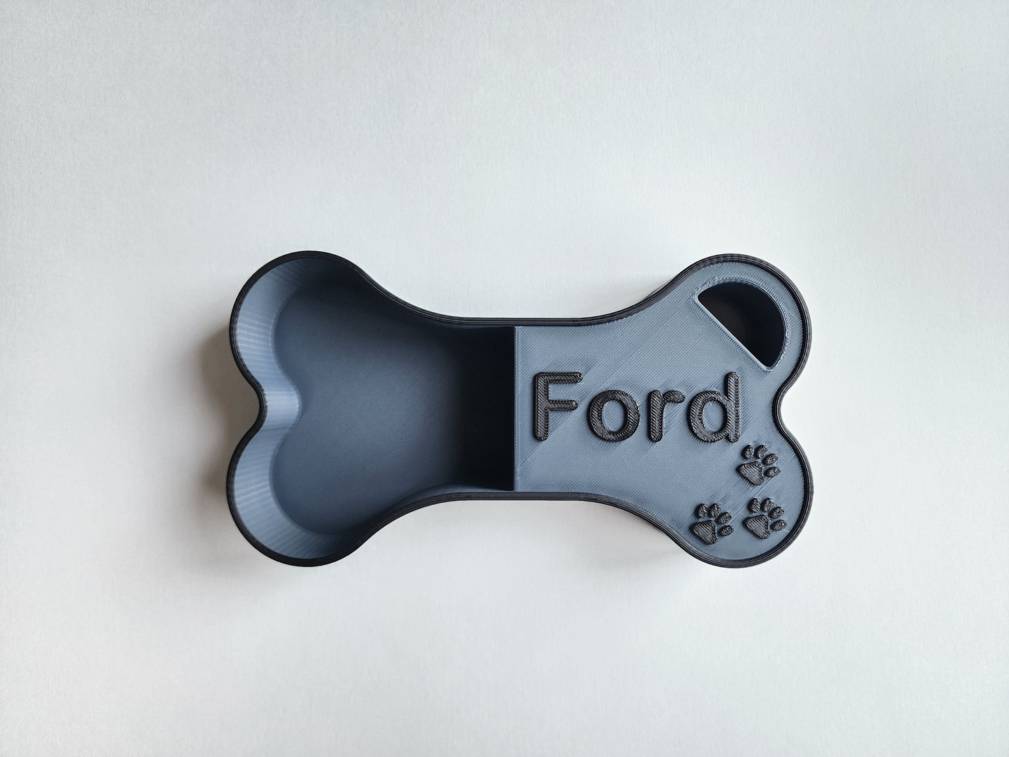 A silver dog food scoop in the shape of a bone with the name Ford in black