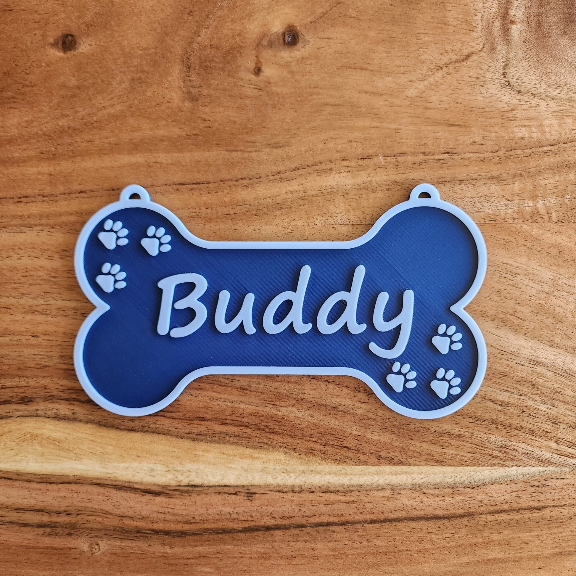 A bone-shaped navy dog crate sign with the name Buddy in white