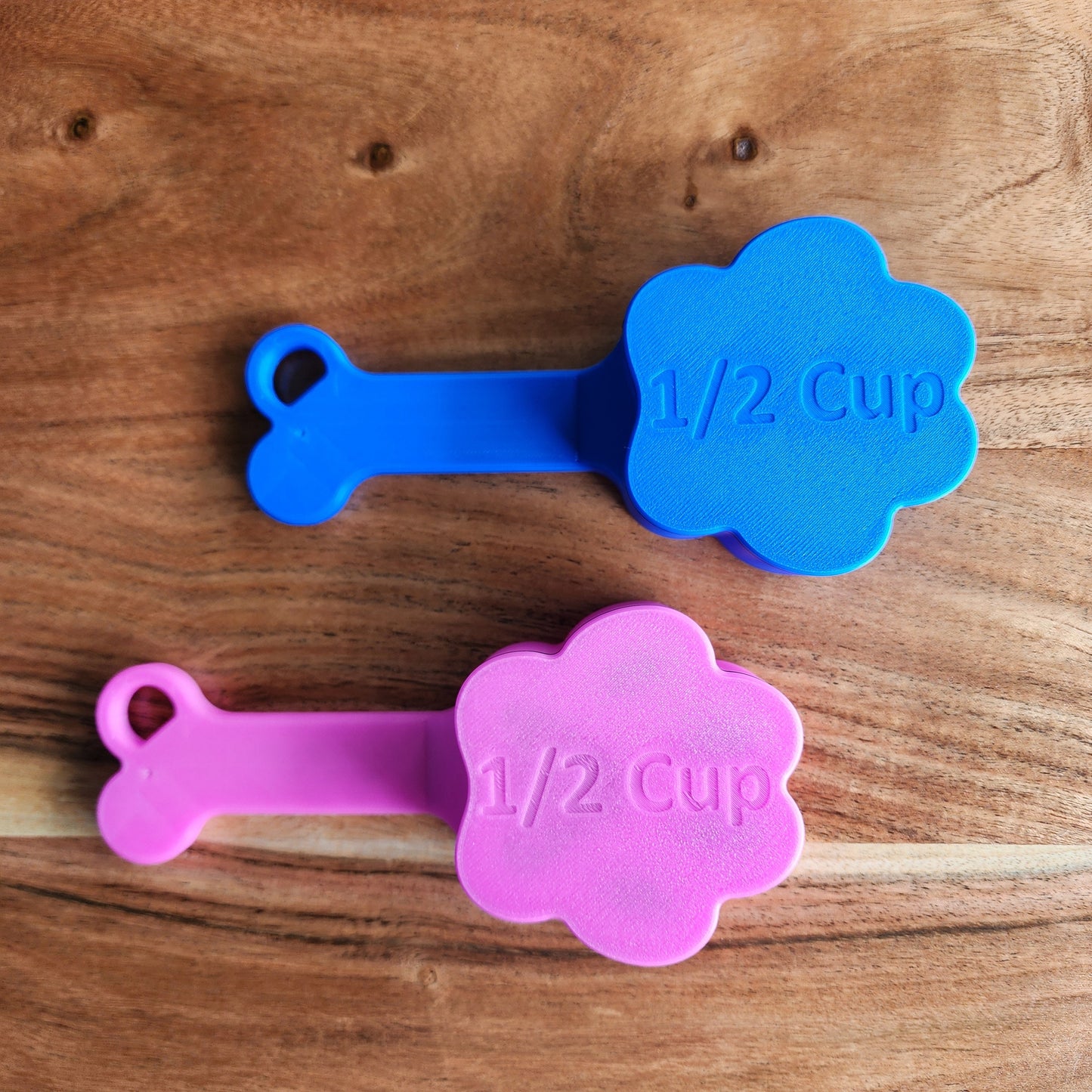 The underside of a blue scoop labeled 1/2 cup and the underside of a fuchsia scoop labeled 1/2 cup.