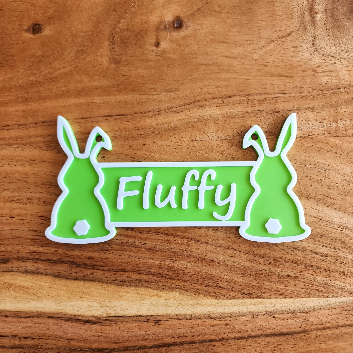 An apple green rabbit cage sign with the name Fluffy in white.